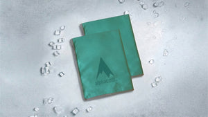 Two teal AlphaCool cooling towels with scattered ice cubes on a crisp grey surface, promoting instant refreshment.