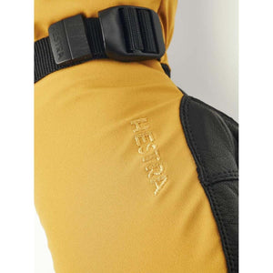 Yellow mittens by Hestra with black leather palm, embroidered Hestra logo, and a black buckle strap.