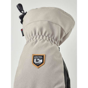 Light gray 3-finger glove by Hestra with an embroidered shield logo, gathered wrist, and black clip.