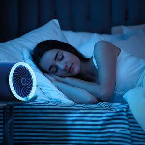 A young woman sleeps peacefully in a dimly lit bedroom, illuminated by the soft blue glow of a circular fan on her bedside table.