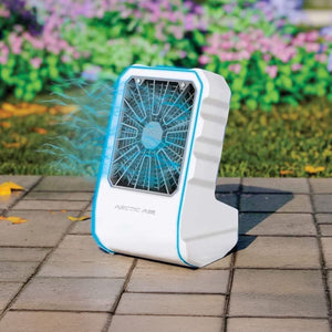 White and blue 'ARCTIC AIR' portable cooler blowing cool blue air on a paved patio, with a vibrant garden in the background.