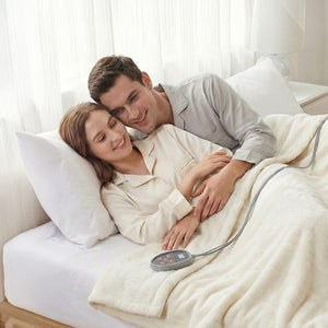 A smiling man embraces a woman in light pajamas in bed, under a cream heated blanket with a gray controller.