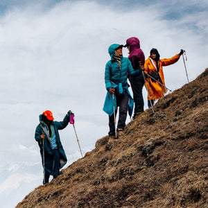 Four hikers ascend a steep, brown, grassy hillside under a cloudy sky.