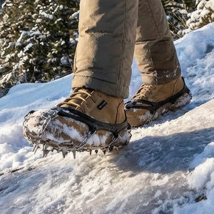 Person wearing tan E-Zred boots with black ice cleats walks on a bright, snow and ice-covered winter trail.