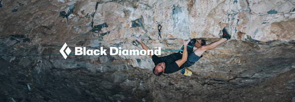 Black Diamond logo and text above a male climber in black traversing a textured rock overhang, with a blue rope and climbing gear visible.