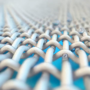 Close-up microscopic view of tight, beige fabric weave showing criss-crossing fibers over a bright blue background, with tiny water droplets.