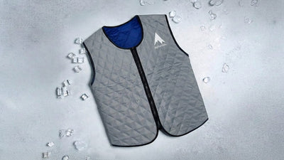 A gray quilted alphacool cooling vest with blue lining and zipper lies on a cold, light surface with scattered ice cubes and water droplets.