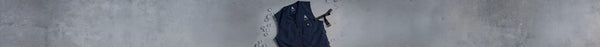 A navy blue zippered cooling vest with a white mountain logo and black strap lies on a gray surface, surrounded by scattered clear ice cubes.