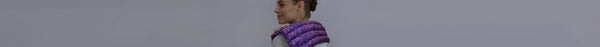 A woman in a purple quilted vest smiles, looking left against a solid light grey background.
