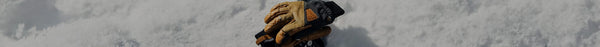 A pair of brown leather and black Thinsulate gloves rests on a pristine, textured white snow surface under bright light.