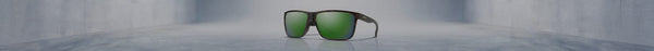 Smith sunglasses with dark frames and vibrant green reflective lenses sit centered on a glossy grey floor in an empty, wide concrete room.