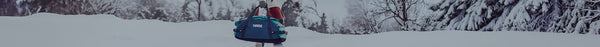 Person walking through a snowy winter landscape, carrying a teal duffel bag with the 