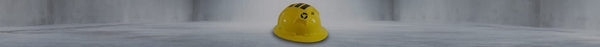 A yellow hard hat with black stripes and a black swirling logo rests upside down on a light grey floor in a blurred room.