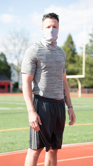 Grey cooling neck gaiter by AlphaCool, worn by a man over his mouth and neck on a running track.