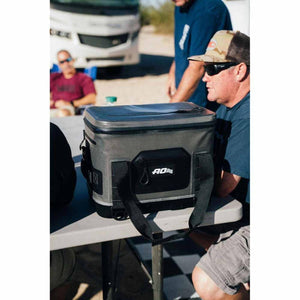 Grey Hybrid 24 Can Pack Cooler by AO Coolers with a black front pocket and strap, on a table outdoors.