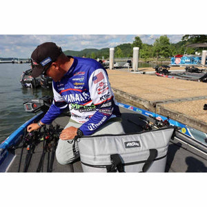 Grey soft-sided cooler by AO Coolers with black straps and buckle on a fishing boat deck with fishing rods.