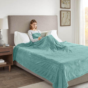 A teal microlight heated blanket by Beautyrest, with a subtle striped texture, covering a woman reading in bed.