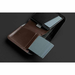 Brown leather Note Sleeve by Bellroy, open to show a black interior and grey cards sliding out.
