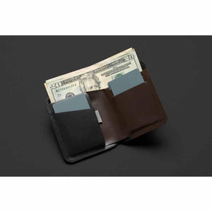 Open dark leather note sleeve by Bellroy, showing brown interior with twenty-dollar bills and two cards.