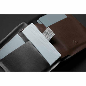 A brown and black leather Note Sleeve by Bellroy, open, holding light blue cards, with a woven grey pull tab and debossed owl logo.