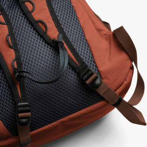 Rust-colored daypack by Bellroy, showing a dark grey mesh back panel and adjustable black straps with brown webbing.
