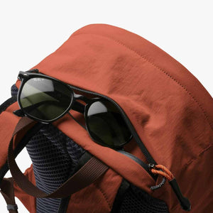 Burnt orange daypack from Bellroy with a black zipper, mesh back panel, and black sunglasses in the open top pocket.