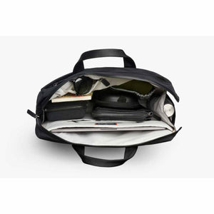 Black work bag by Bellroy, open from a top-down view revealing a laptop, two zippered pouches, book, sunglasses, and water bottle.