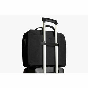 Black work bag by Bellroy, strapped to a silver rolling luggage handle with a black strap.