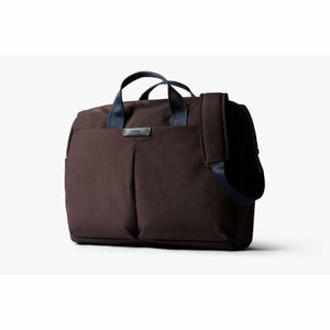 Dark brown fabric work bag by Bellroy with blue handles, a shoulder strap, and a front pocket label.