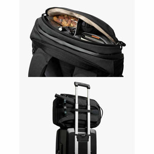 Black 20L Venture Ready Pack by Bellroy with its top compartment open and attached to a rolling suitcase handle.