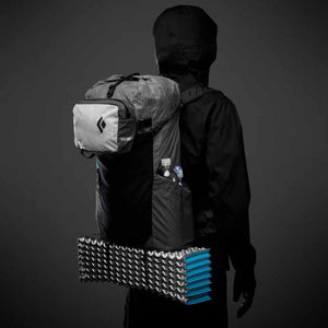 Grey Beta Light 30 backpack by Black Diamond, worn on a person's back, with a front logo pouch, side water bottle pockets, and a blue sleeping pad attached.