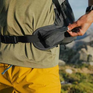Black grid pattern backpack by Black Diamond, showing a hip pouch being unzipped.