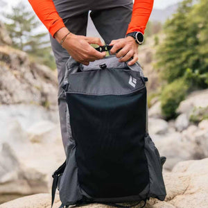 Black and gray grid pattern backpack by Black Diamond, being fastened by hands in an outdoor setting.