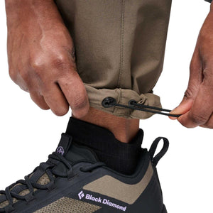 Khaki Women's Alpine Hybrid Pant by Black Diamond, with hands adjusting the elastic drawcord cuffs above a dark shoe.