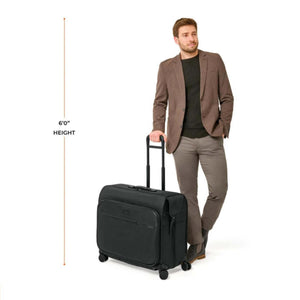 Black Deluxe Wardrobe Spinner by Briggs & Riley, with extended handle, next to a casually dressed man.