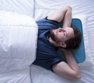 Blue rectangular cooling pad by Cool Care Technologies cushioning a sleeping man's head on a white bed.