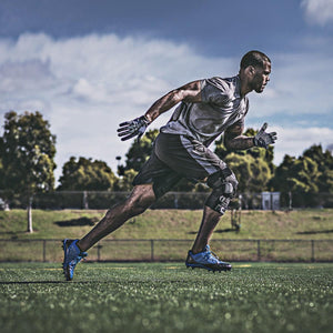 Black orthopedic knee brace by DonJoy securing a man's right knee as he sprints on a green field.