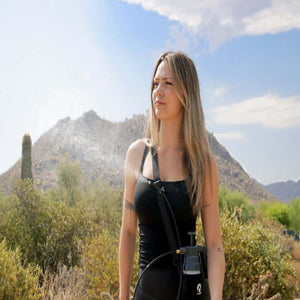 Black personal mister by ExtremeMIST spraying a fine mist, carried by a woman in a desert landscape.