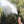 Black personal mister by ExtremeMIST spraying a fine mist, held by a hand against green bushes.