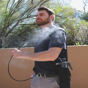 Personal mister by ExtremeMIST spraying a fine mist onto a man's chest, with the pump unit in a black side holster.