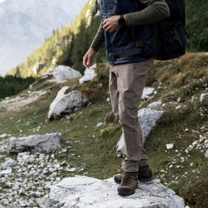 Khaki men's Abisko Trail Trousers by FjallRaven, worn by a man hiking in a rocky outdoor landscape.