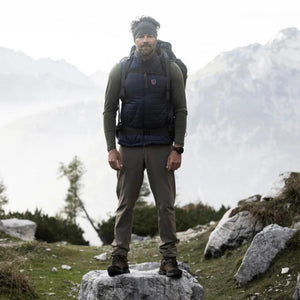Khaki men's Abisko Trail Stretch regular trousers by FjallRaven, worn by a man on a rock.