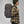 Dark olive robust backpack by FjallRaven with brown leather trim and front lacing, worn by a person in a plaid shirt and beanie, side view.