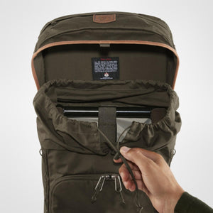 Dark olive robust backpack by FjallRaven with an open top, drawstring closure, and a hand pulling the cord.