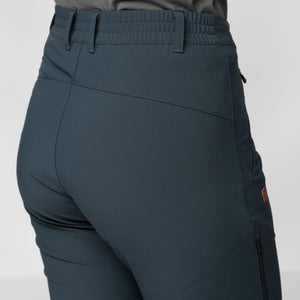 Dark blue women's trail stretch trousers by FjallRaven with an elasticated back waistband, paneled design, zipped side pocket, and logo patch, viewed from the back.