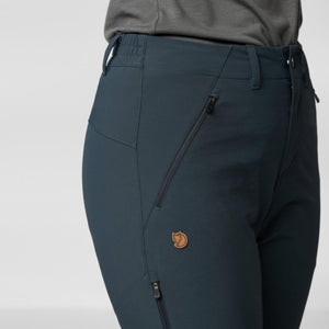 Dark blue-grey stretch women's trousers by FjallRaven with diagonal zipped pockets and a fox logo.