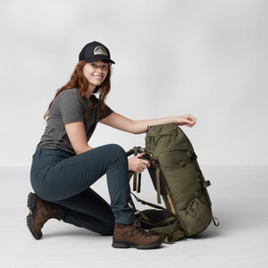 Dark teal women's trousers by FjallRaven, with a zippered thigh pocket, worn by a woman kneeling.