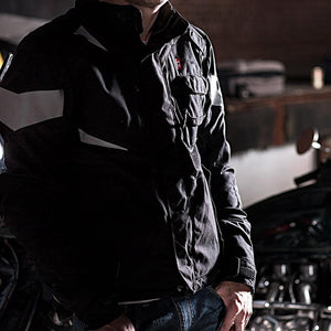 Black motorcycle heated jacket by Gerbing, with reflective grey panels and multiple utility pockets, worn by a person.