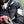 Black Motorcycle Heated Jacket by Gerbing, worn by a rider in a helmet and gloves, holding a red phone, with white accents and logos.