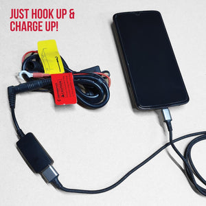 Black 12V to USB charger cable by Gerbing, with red and yellow tags, featuring ring terminals and an attached braided USB cable charging a black smartphone.